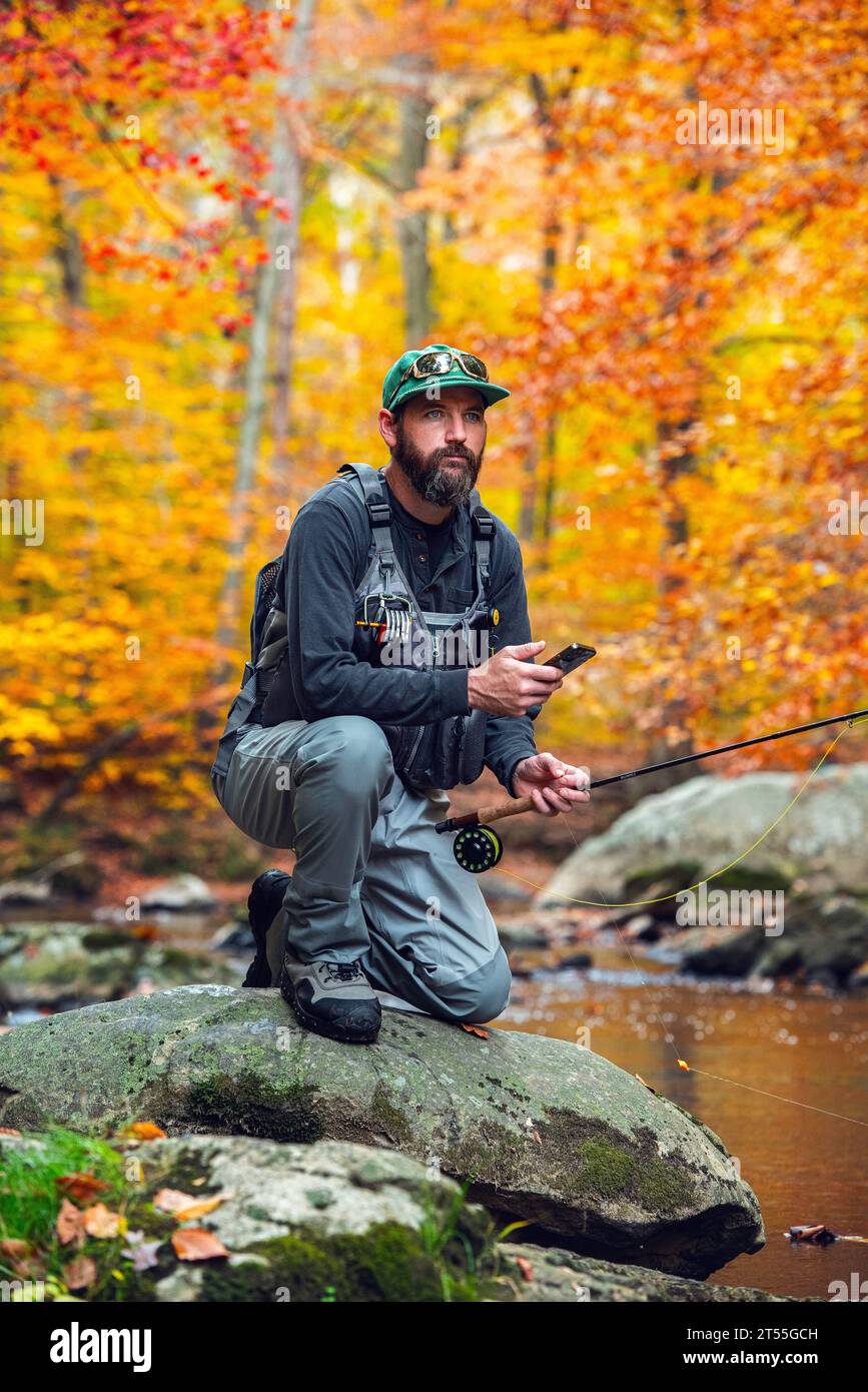 Man checking phone while fly fishing on a colorful fall day Stock Photo