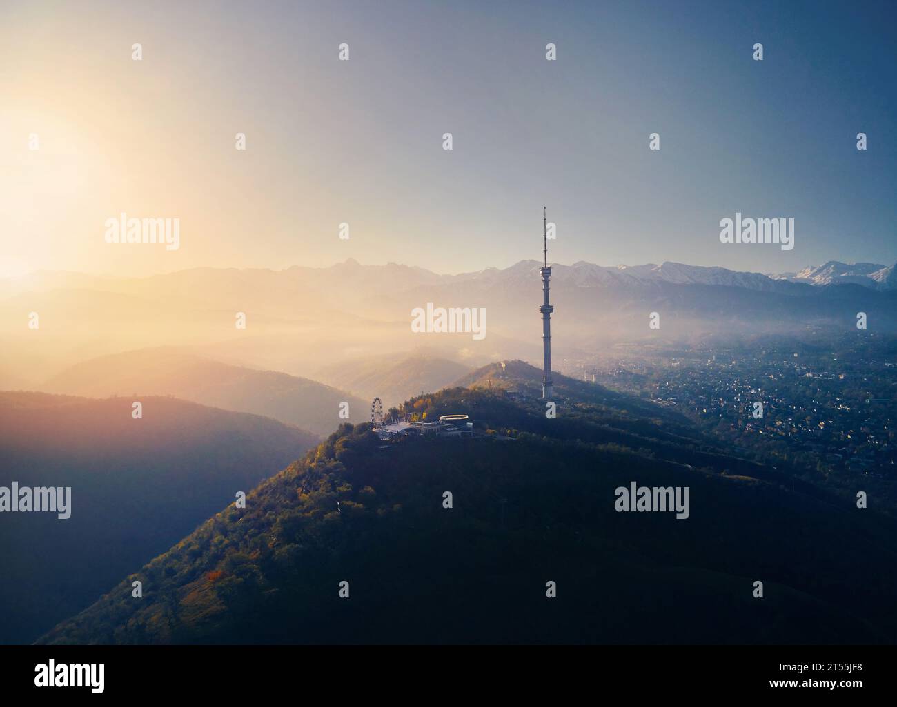 Aerial drone shot of symbol Almaty city high TV tower and park at Koktobe hill against snow mountains at sunrise in Kazakhstan Stock Photo