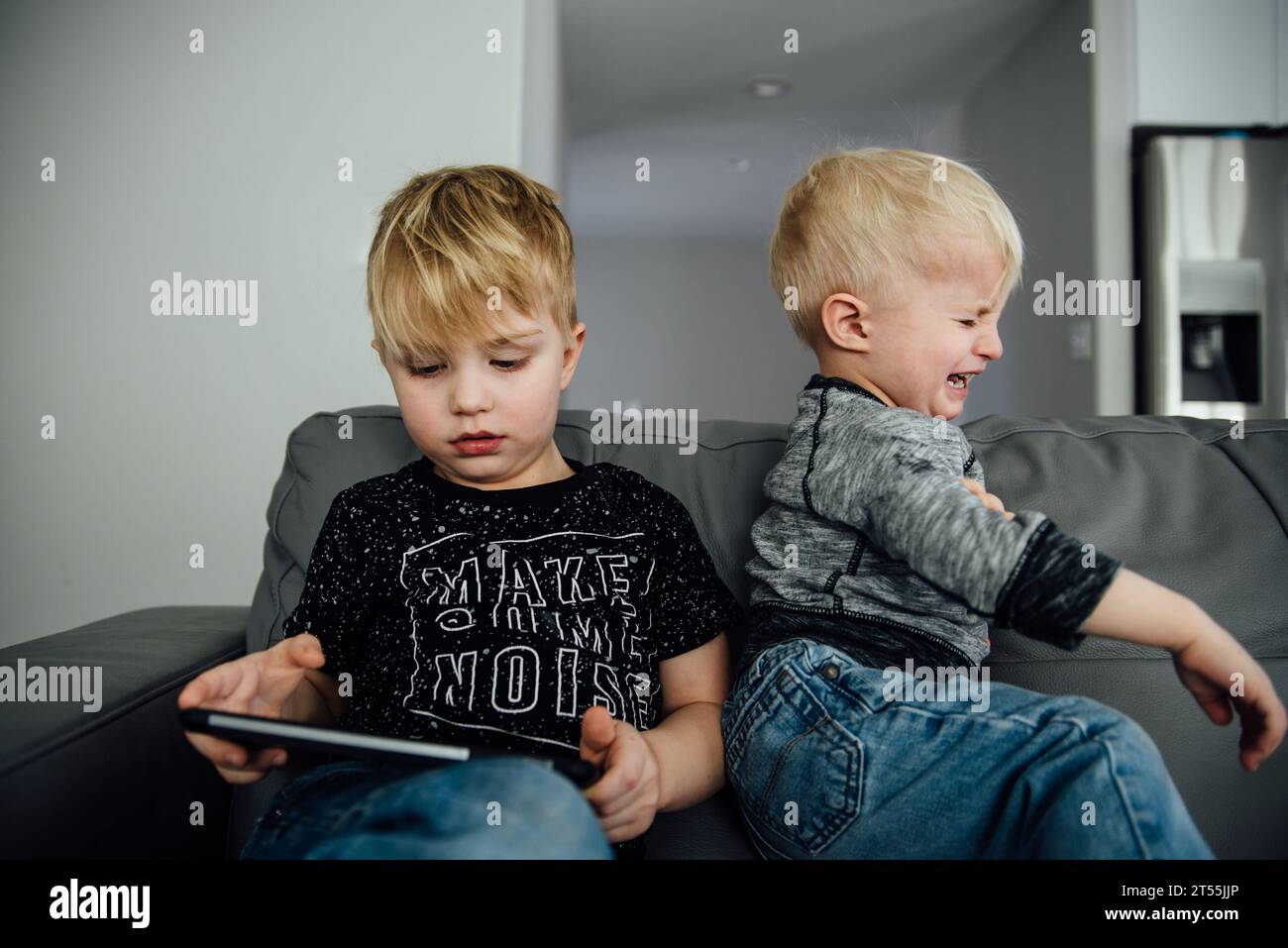 Two boys sit on a couch while one holds an ipad and the other th Stock Photo