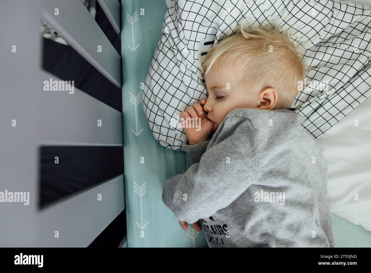 Overhead shot of little boy sleeping on side in crib sucking his Stock