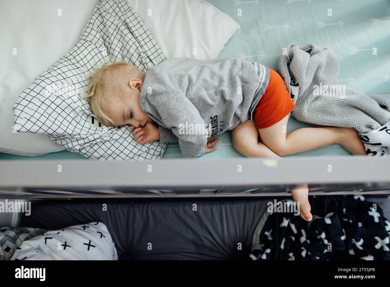 Overhead shot of little boy sleeping on side in crib sucking his Stock