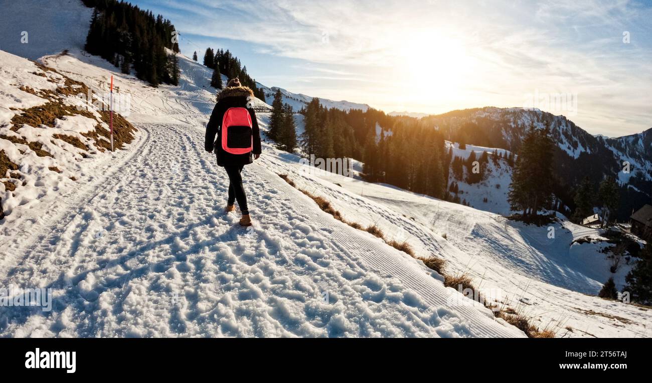 Young woman walking on snow mountain track during winter time at sunset - Travel and landscape nature concept - Focus on body Stock Photo