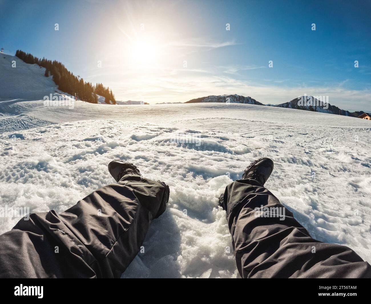 Legs view of young man looking the sunset on snow high mountains - Travel influencer creating content for his social network profile - Winter vacation Stock Photo