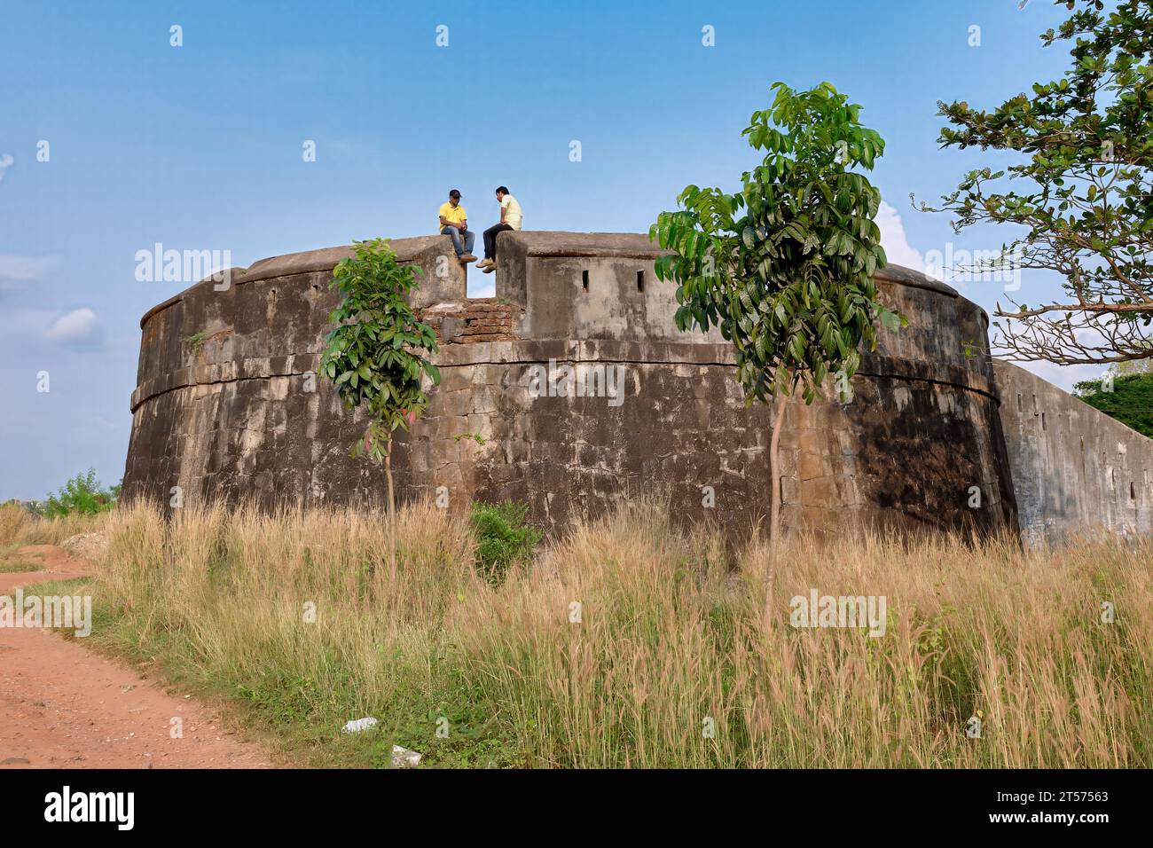 Two Indian men sit on the wall of Sultan Battery,  a watchtower built by Tipu Sultan with the stones of 23 destroyed churches; Mangalore, South India Stock Photo