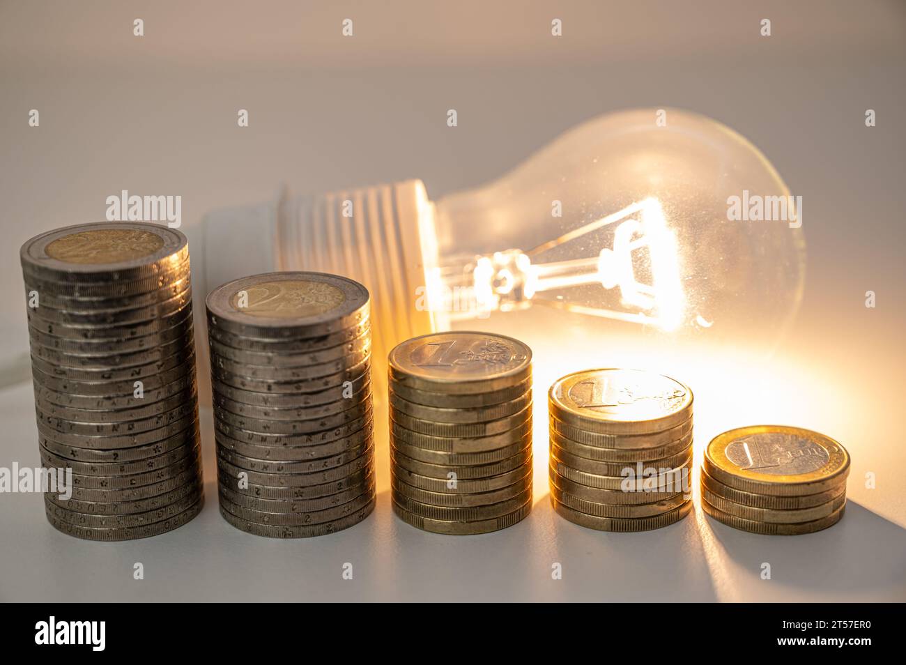 Light bulb lit with stacks of coins of descending height. Reduction in
