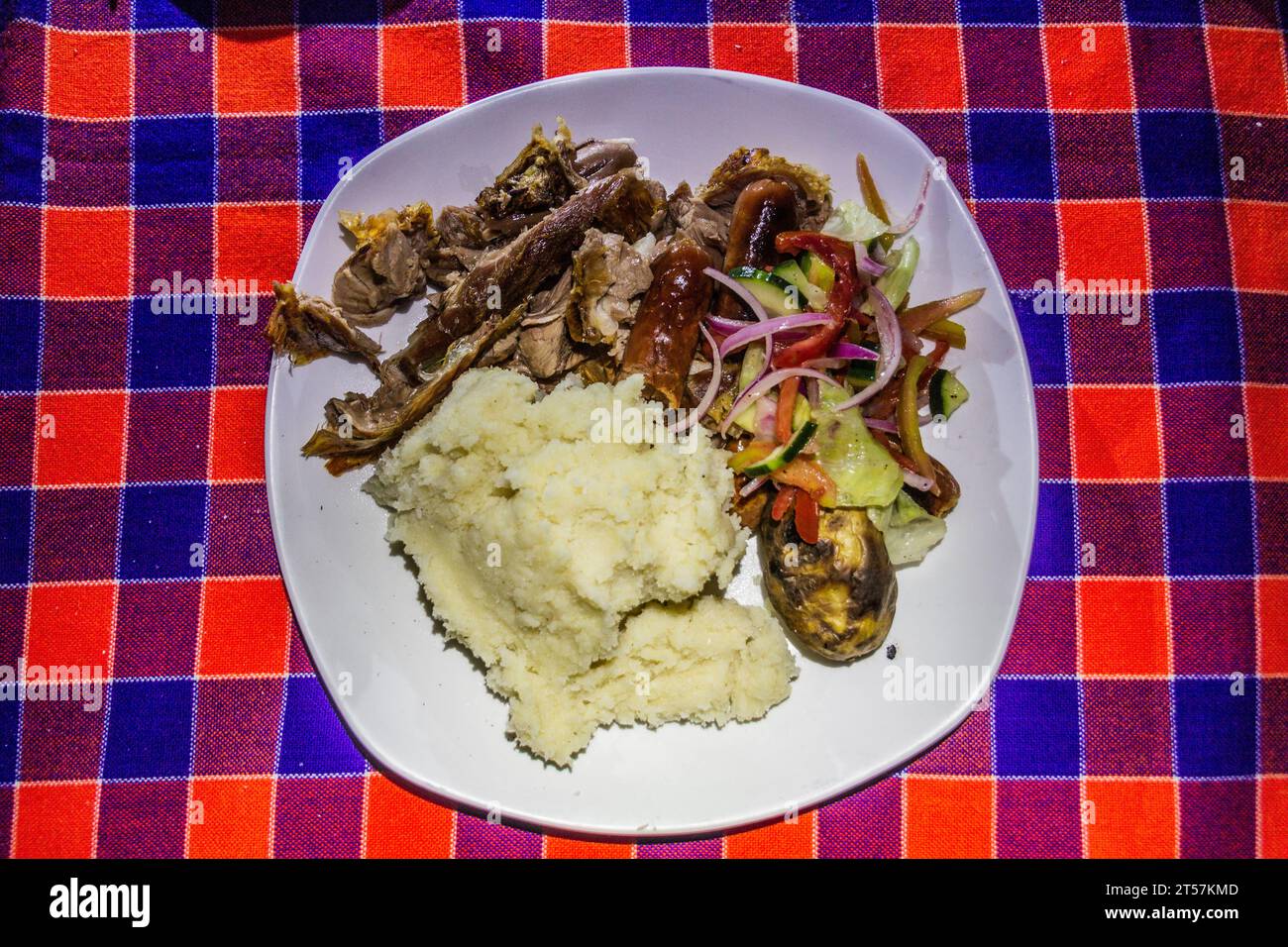 Meal prepared by Masai in Kenya - roasted goat meat, sausages, salad and ugali. Stock Photo