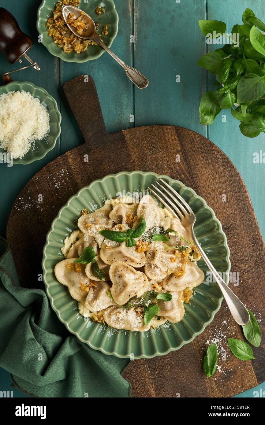 Homemade italian ravioli pasta in heart shape with beef meat, cheese sauce, caramelized onions, basil and saffron on old wooden blue background. Food Stock Photo