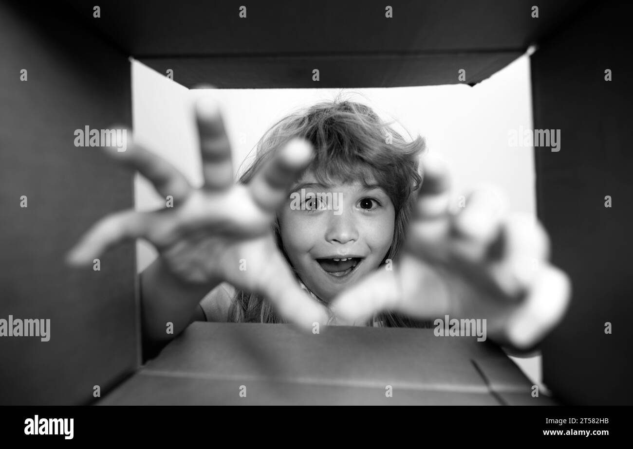 Kid unpacking and opening carton box, and looking inside with surprise face. Child take by hand gift fron open box. Stock Photo
