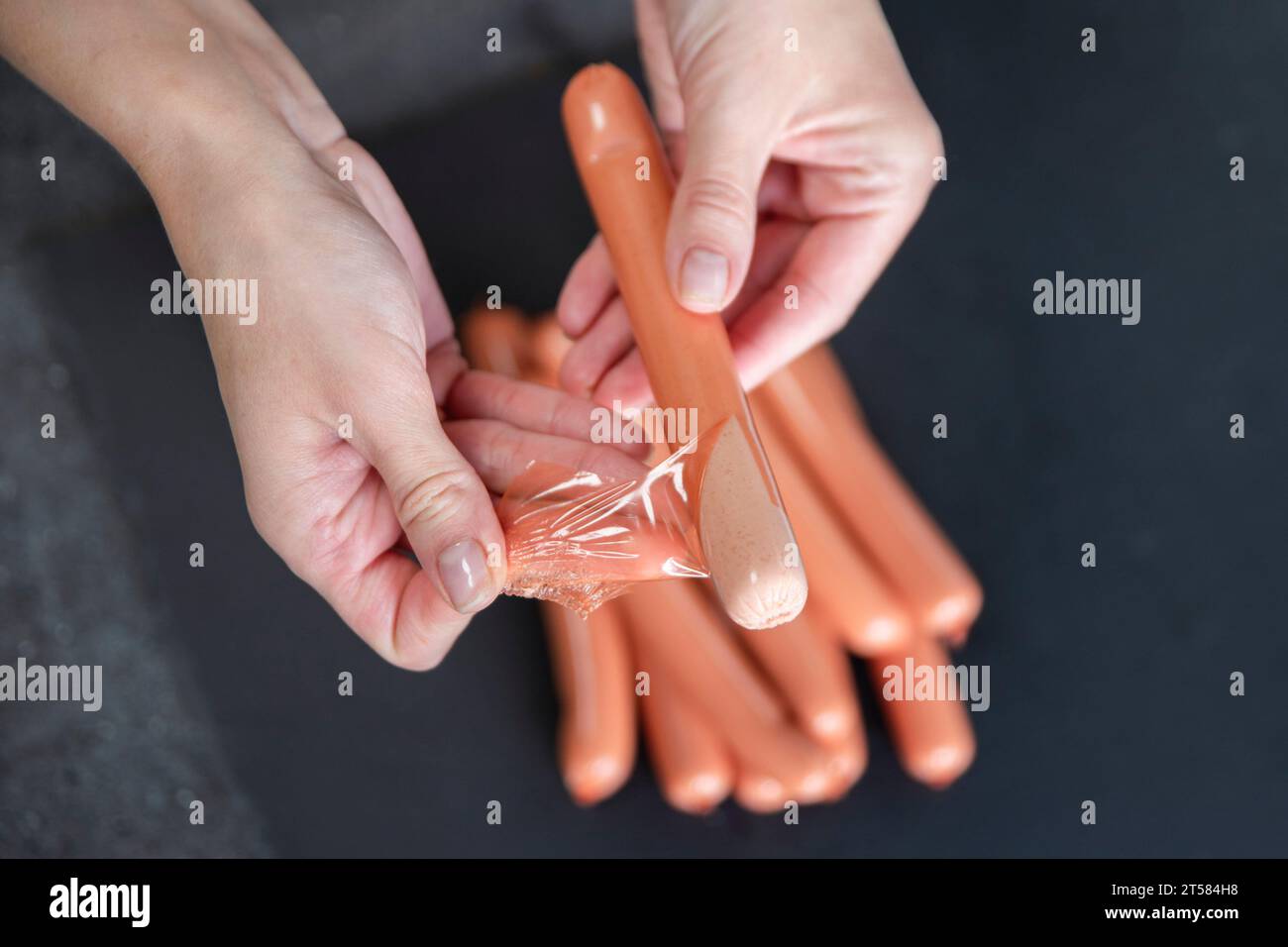 Close-up of a woman removing the skin from a sausage. Preparation for decorating the table for guests. Stock Photo