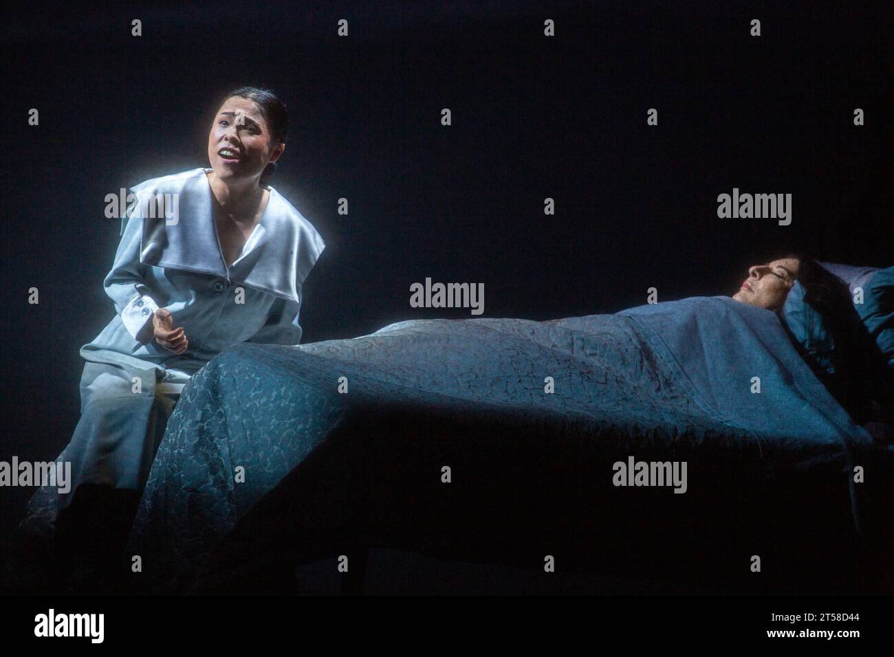 left: Eri Nakamura (as Violetta in La traviata by Verdi) with Marina Abramovic (as Maria Callas asleep in bed) in 7 DEATHS OF MARIA CALLAS at English National Opera (ENO), London Coliseum, London WC2  03/11/2023  with music by Marko Nikodijevic  libretto: Petter Skavlan & Marina Abramovic   conductor: Yoel Gamzou  design: Marina Abramovic & Anna Schoetl  costumes: Riccardo Tisci for Burberry  lighting: Urs Schoenebaum  film director: Nabil Elderkin  visual intermezzos: Marco Brambilla  stage director: Marina Abramovic  NB: image shot through gauze screen Stock Photo