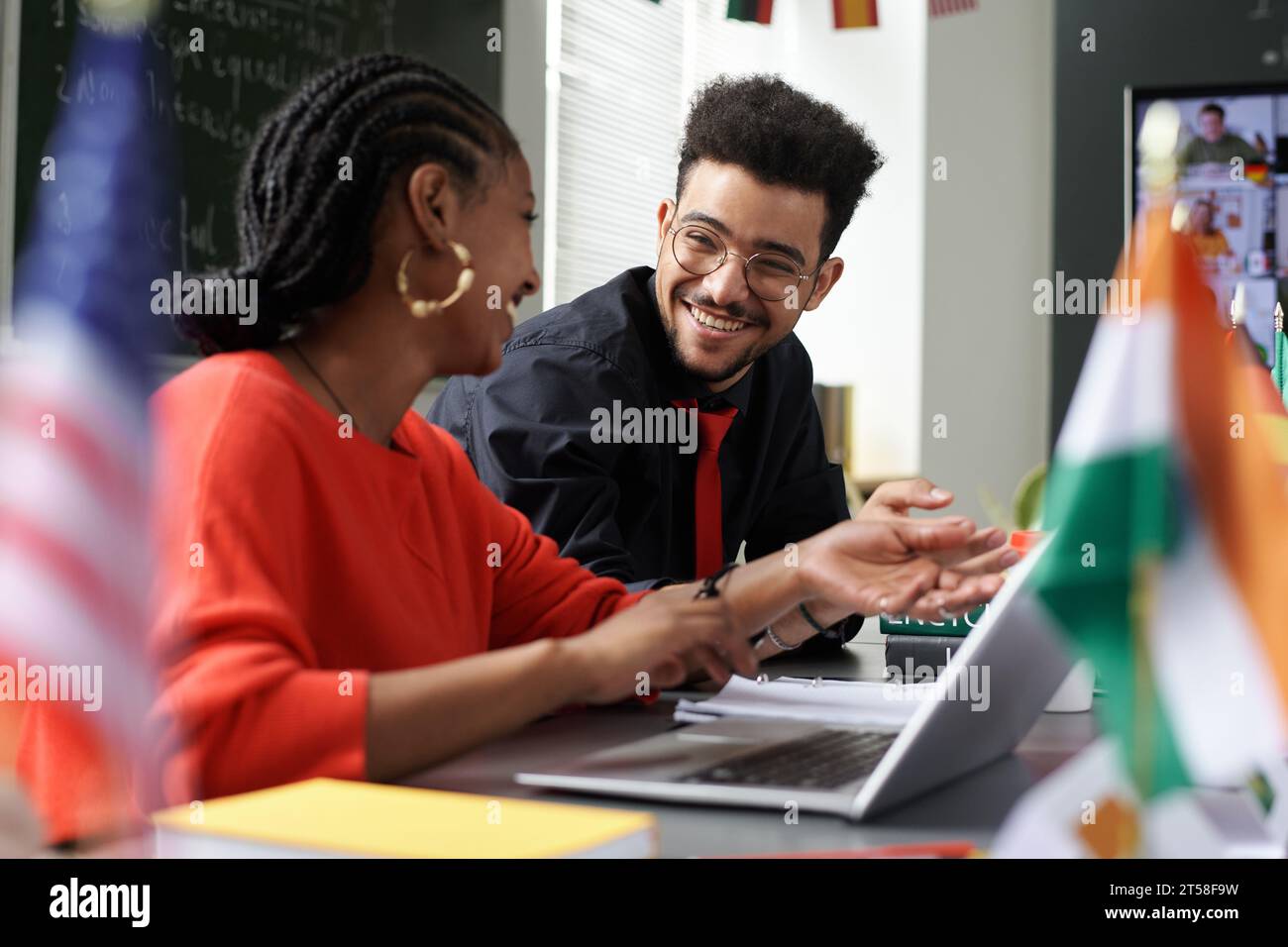 Multiethnic students discussing online work together while sitting at table with laptop Stock Photo