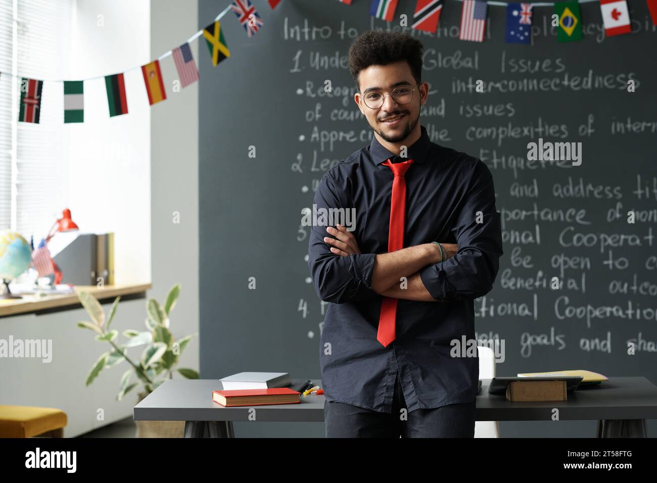 Portrait of Arabic student standing with his arms crossed against the blackboard and smiling at