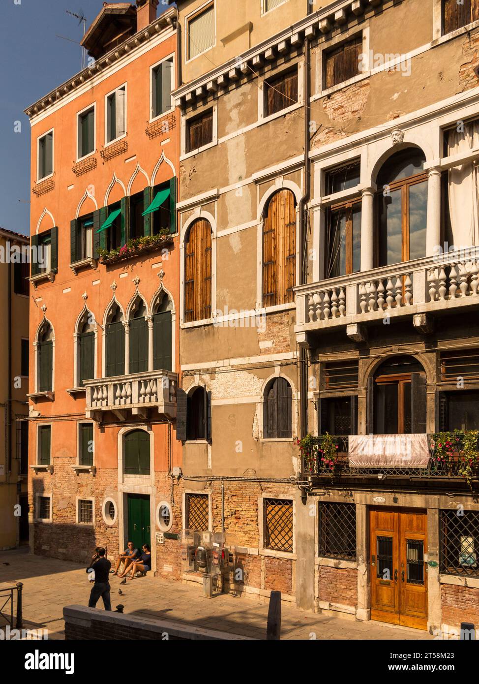 Houses of Venice in Italy. Two people are sitting in a portico while a third person wanders down the street. The ocher color predominates. Stock Photo