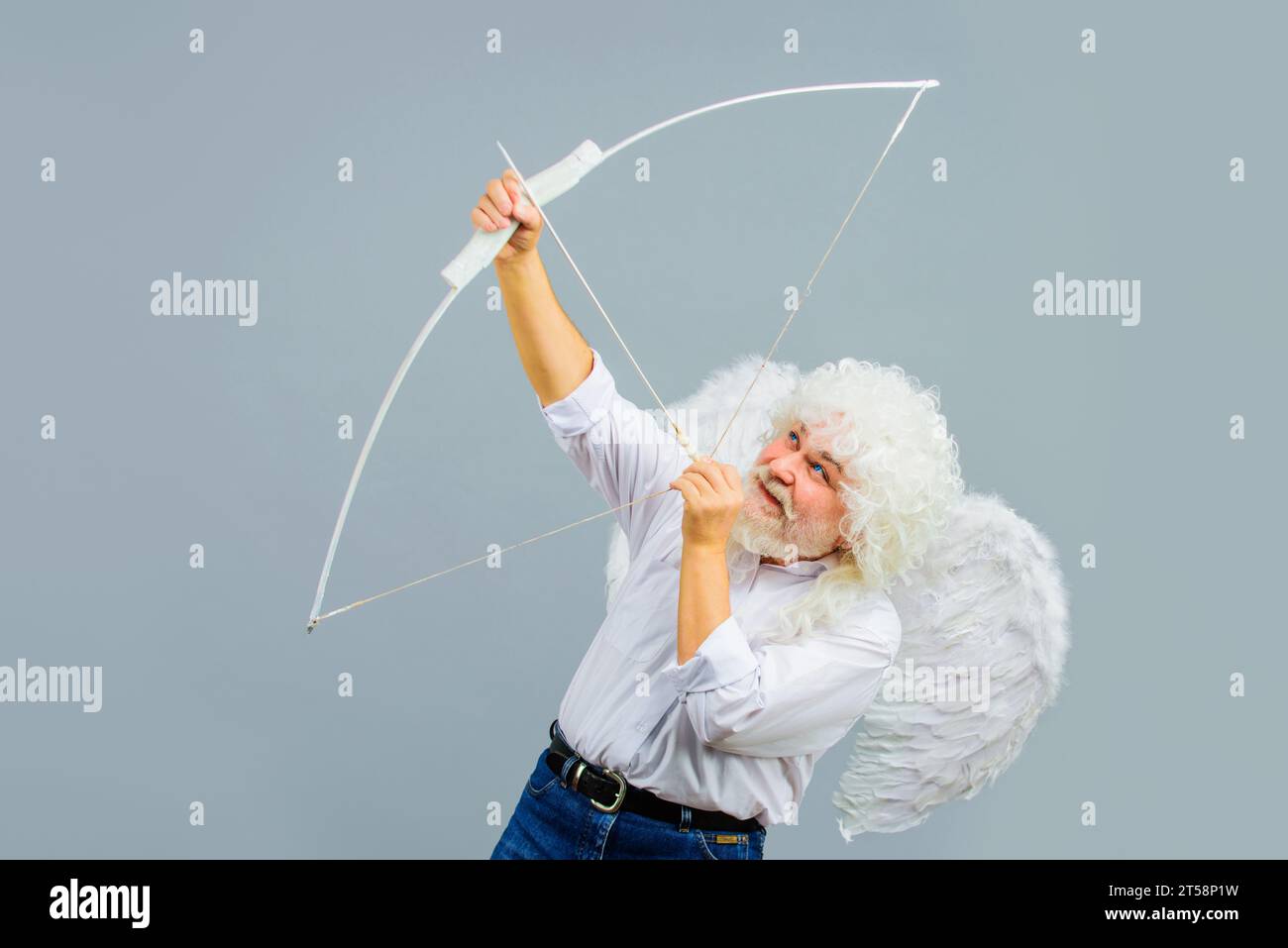 Valentines Day celebration. Arrow of love. Smiling man in white wings and wig shooting love arrow. Valentine angel with white wings shoots love arrow Stock Photo