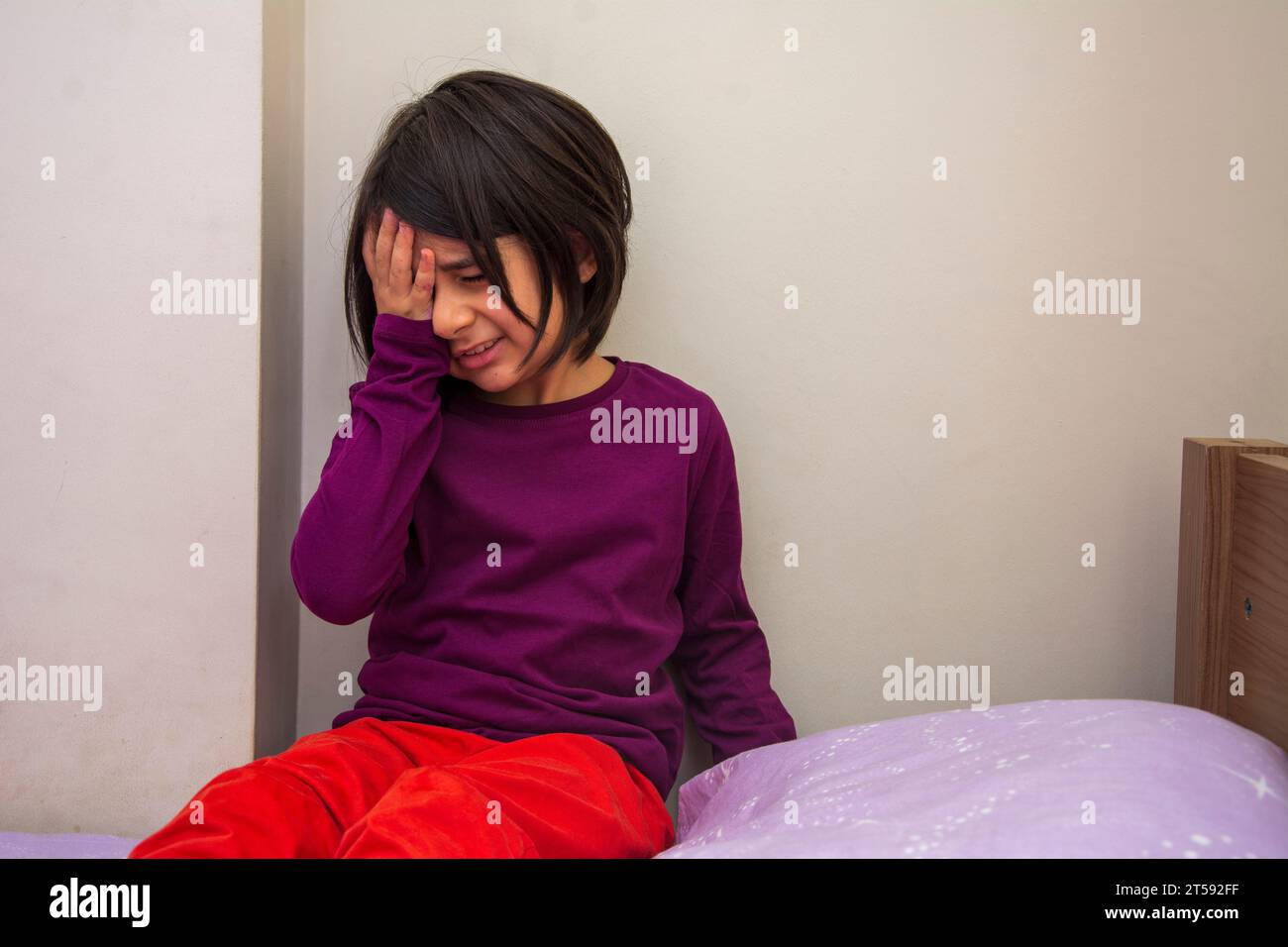 Little girl with headache sits on her bed Stock Photo