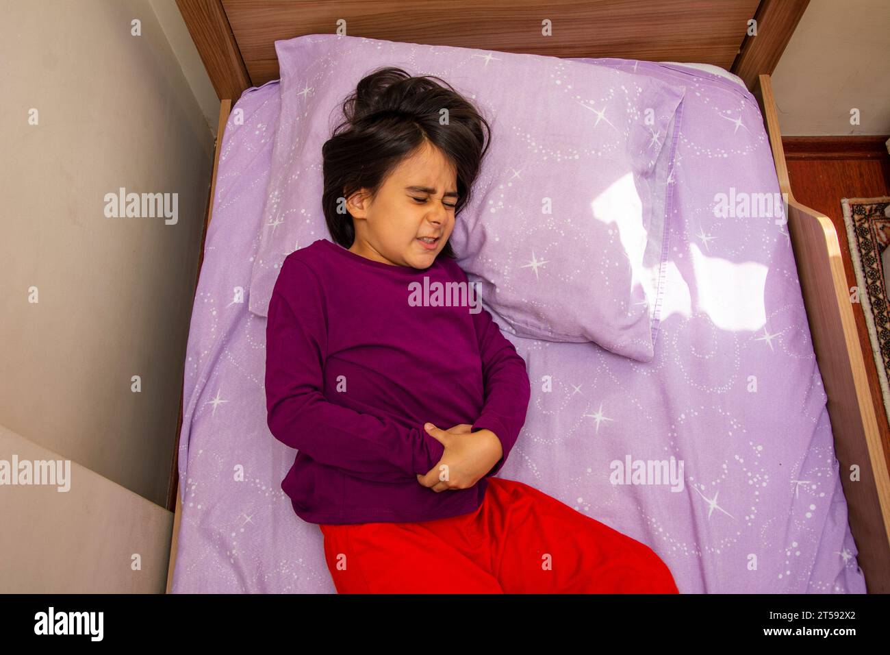 Top view of a little girl lying in bed with abdominal pain Stock Photo