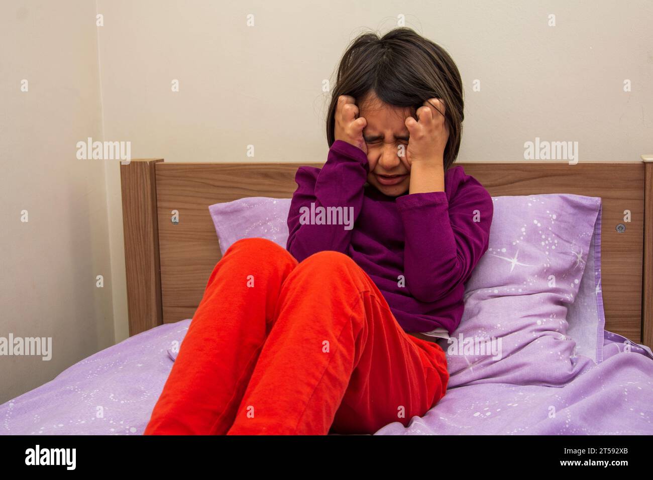 Unable to bear the headache, little girl holds her head with both hands Stock Photo