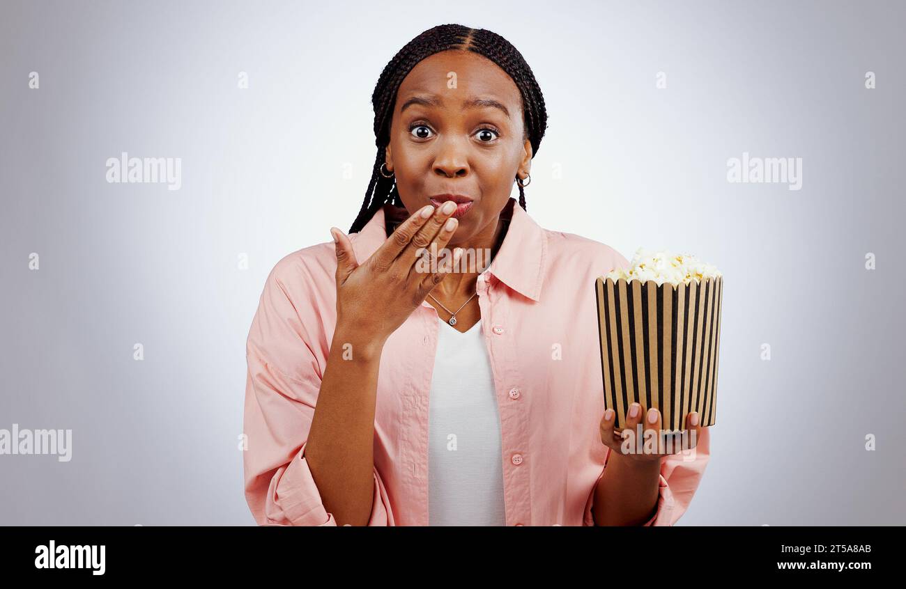 Portrait, surprise or black woman watching movie in studio for cinema with popcorn to relax. Omg, wow or shocked African person eating snack for Stock Photo