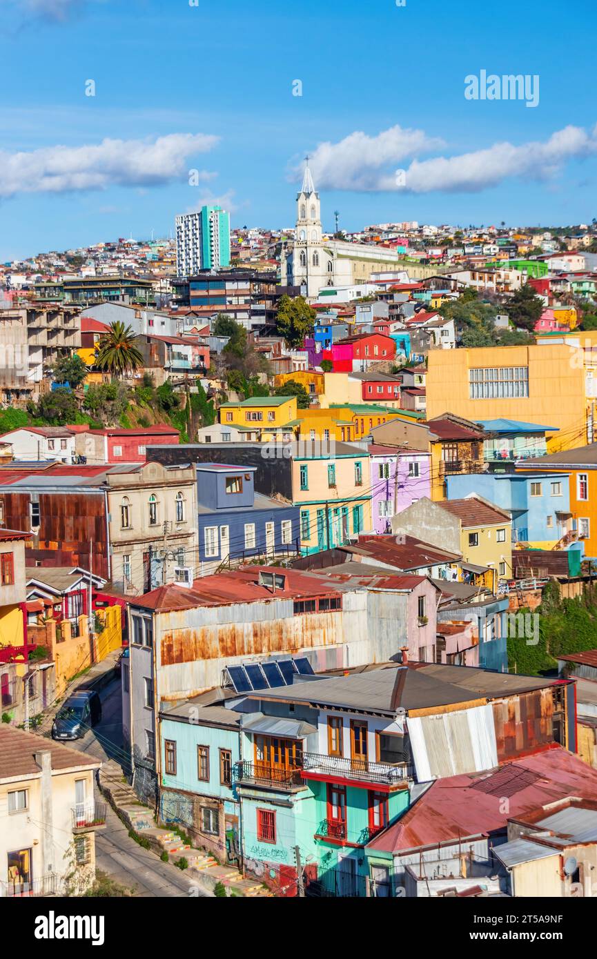 Colourful cityscape of houses and a church in Valparaiso, Chile. The buildings are crammed together and sprawl up the hillside in the winter sun. Stock Photo