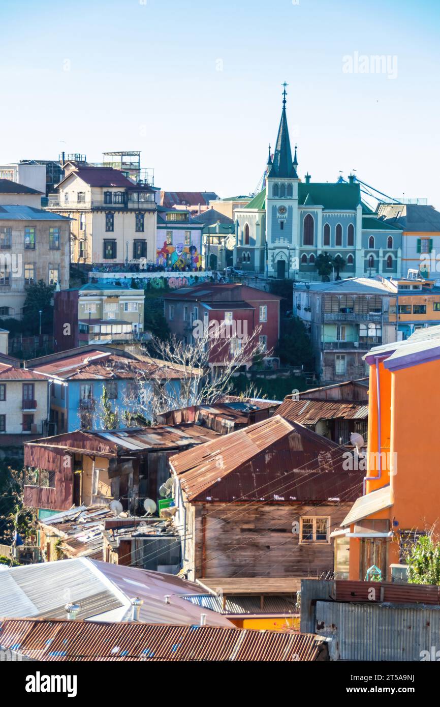 Colourful cityscape of houses and a church in Valparaiso, Chile. The buildings are crammed together and sprawl up the hillside in the winter sun. Stock Photo