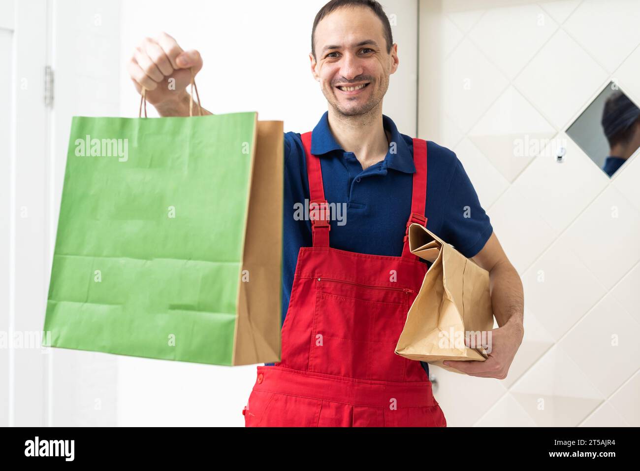 Image of a happy young delivery man in red cap standing with parcel ...