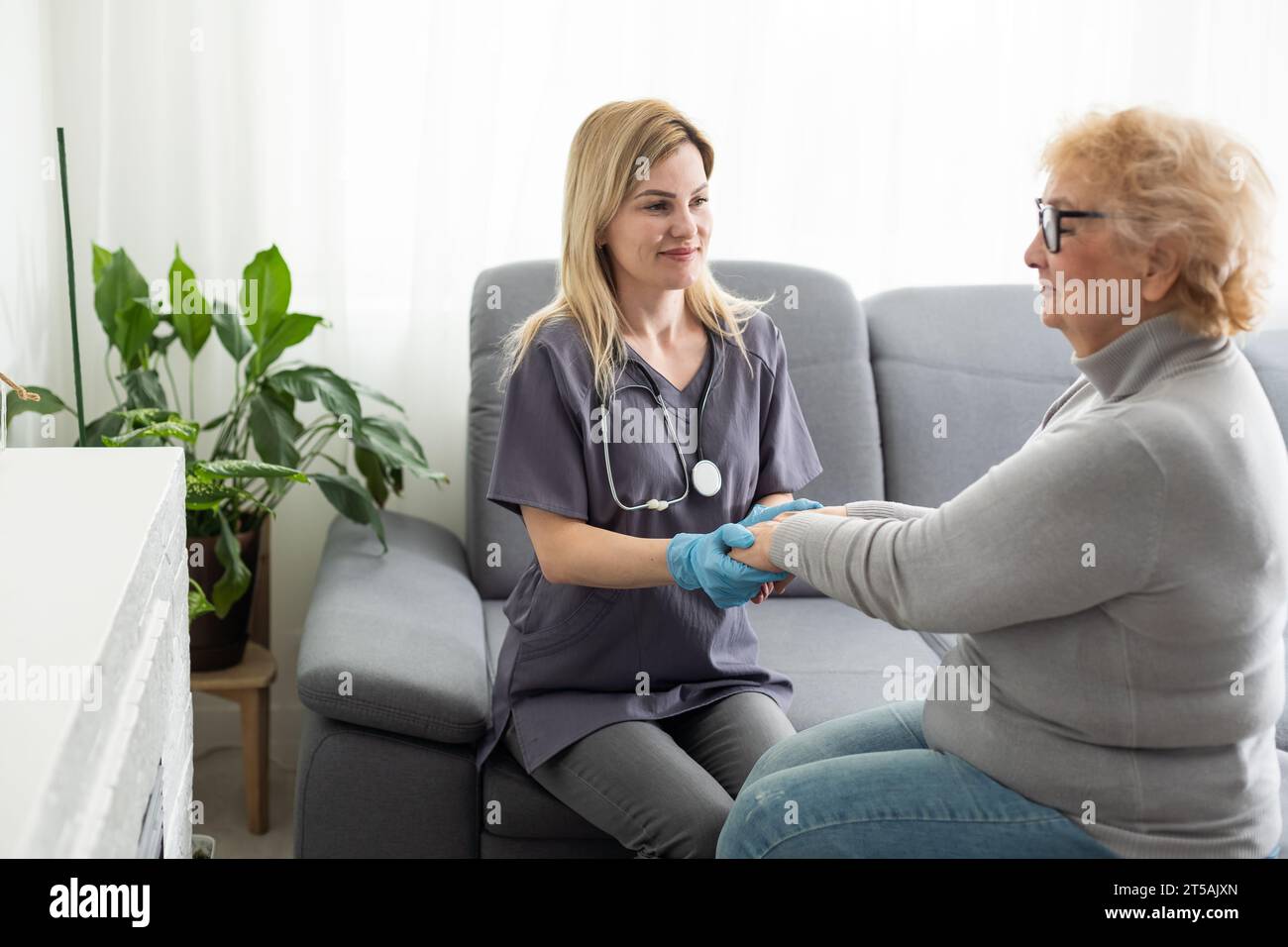 Caring young nurse doctor carer helping holding hands of happy disabled handicapped or injured old adult elder woman having disability health problem Stock Photo