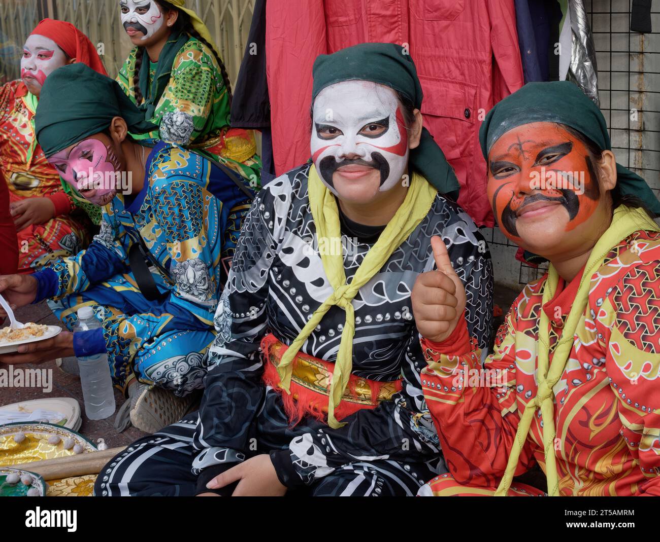 Members of a Lion Dance troupe with exotic dress and colorfully painted faces waiting for their performance at a Taoist shrine in Bangkok, Thailand Stock Photo