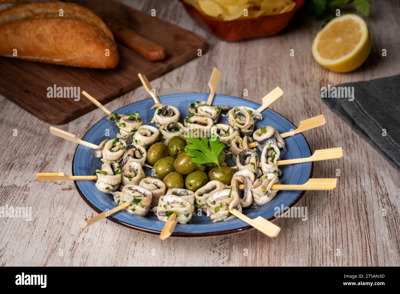 Dish with pickled anchovies pierced on toothpicks and seasoned with garlic and parsley and some olives to accompany. Stock Photo