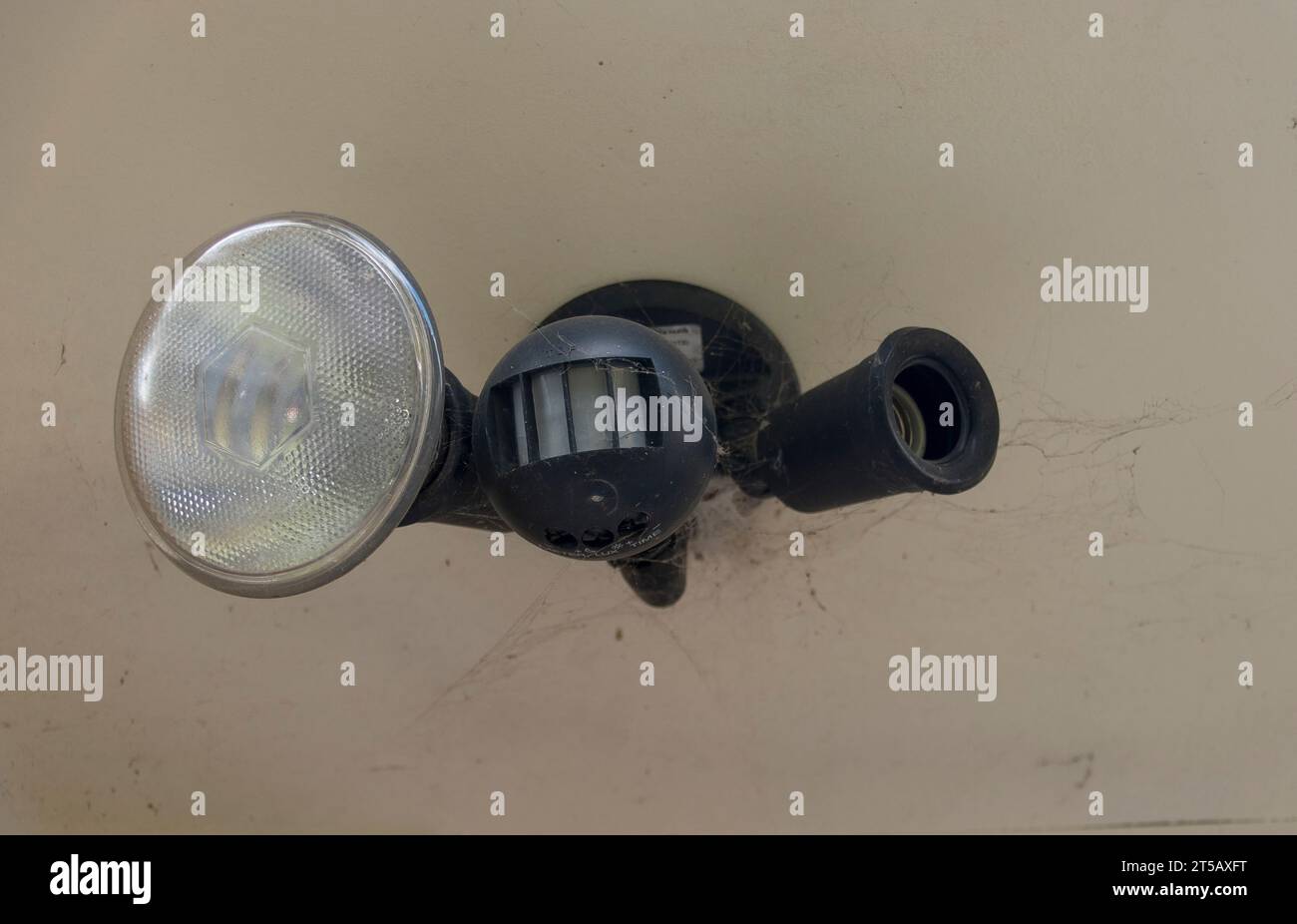 Australian outdoor domestic security motion detector and light fitting with one bulb (globe) removed. About 20 years old. Cobwebs round fitting. Stock Photo