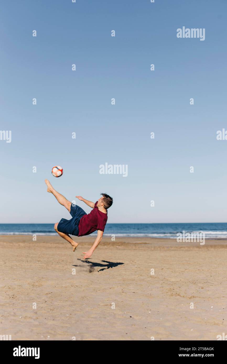 Guy playing football beach Stock Photo