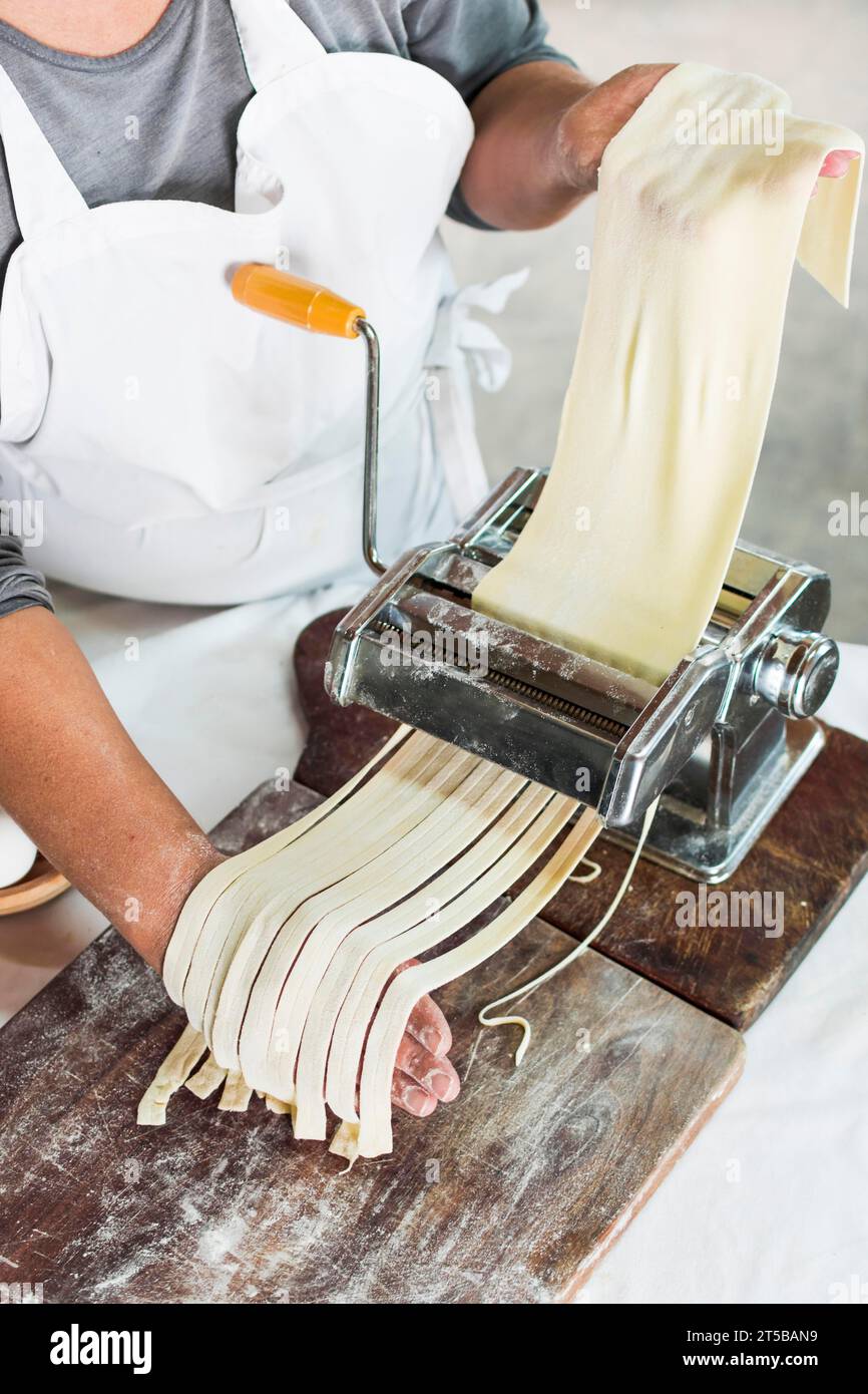 Close up baker cutting raw dough into tagliatelle pasta machine Stock Photo