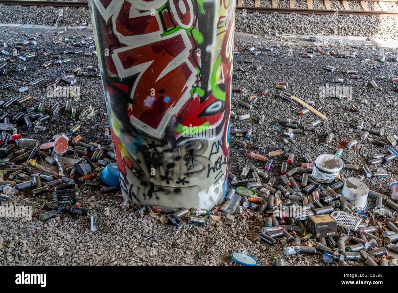 Empty spray paint cans, on a railway track below a road bridge, thrown