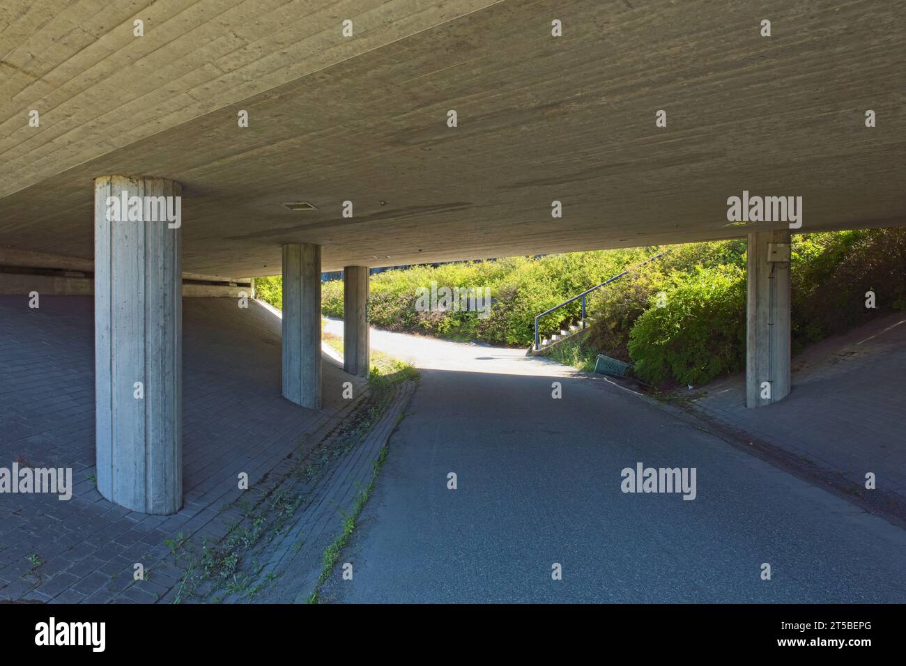 Asphalt coated walkway going under concrete bridge in sunny summer weather. Stock Photo