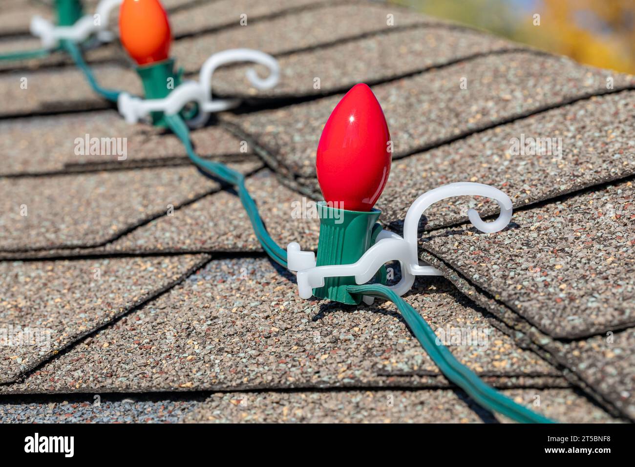 Hanging Christmas string lights on shingles of roof. Holiday decorating safety, lighting and accident prevention concept. Stock Photo