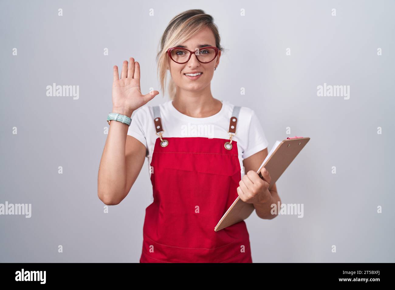 Hello Waitress Young blonde woman wearing waiter uniform holding clipboard waiving ...