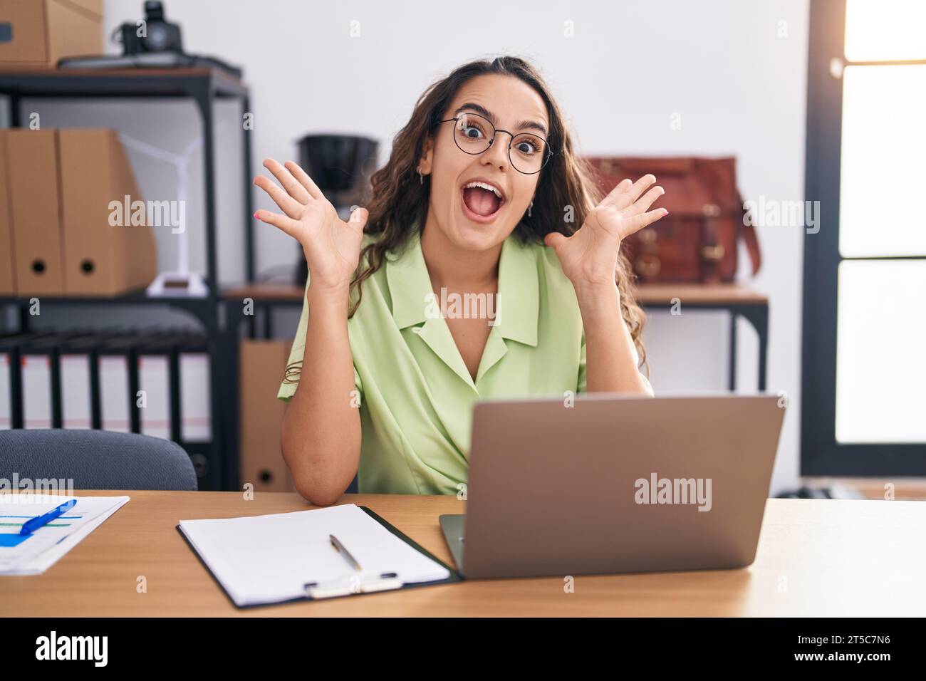 Young hispanic woman working at the office wearing glasses celebrating ...