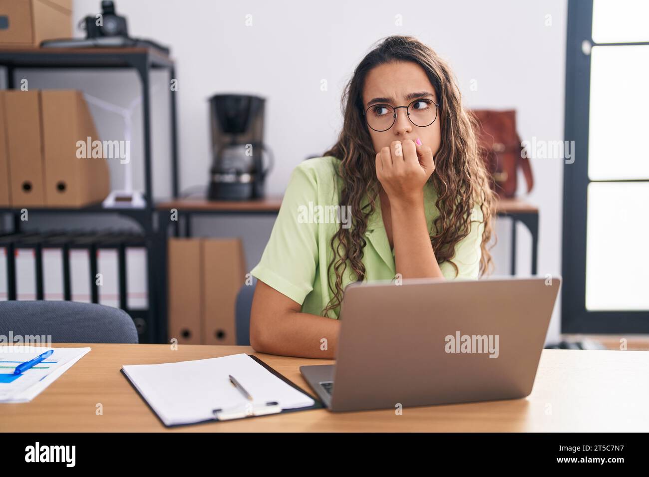 Young hispanic woman working at the office wearing glasses looking ...