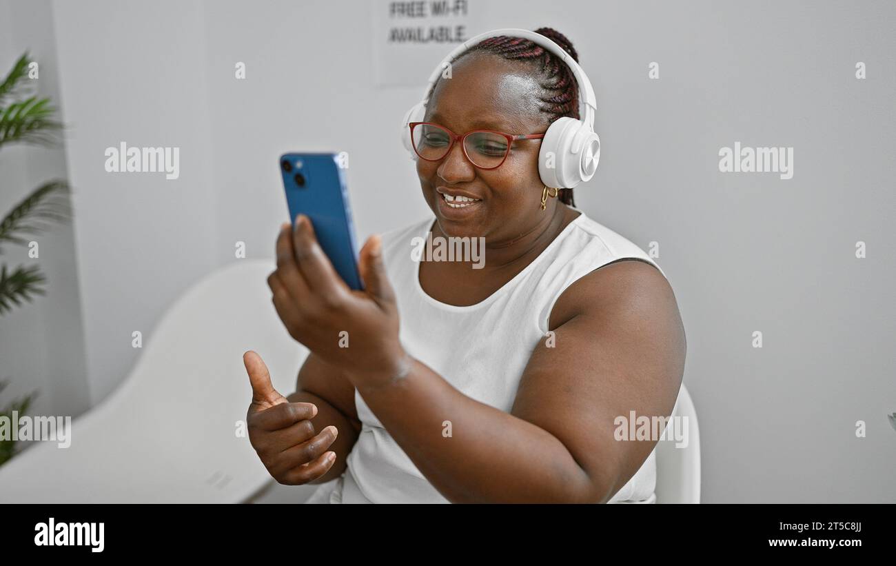 Confident african american woman, joyously smiling while having a business video call in the waiting room, sitting comfortably, adding soulful rhythm Stock Photo