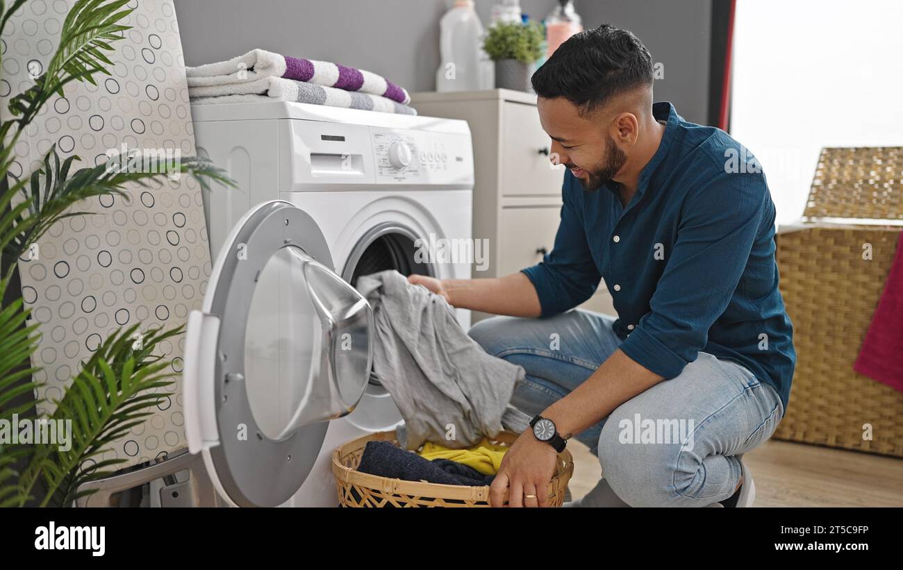 Young hispanic man doing laundry with washing machine at laundry room Stock Photo