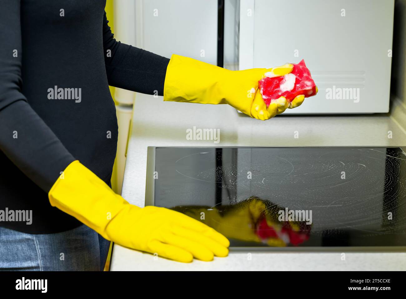 woman in rubber gloves washes the hob in the kitchen. washing the hob in the kitchen. Stock Photo