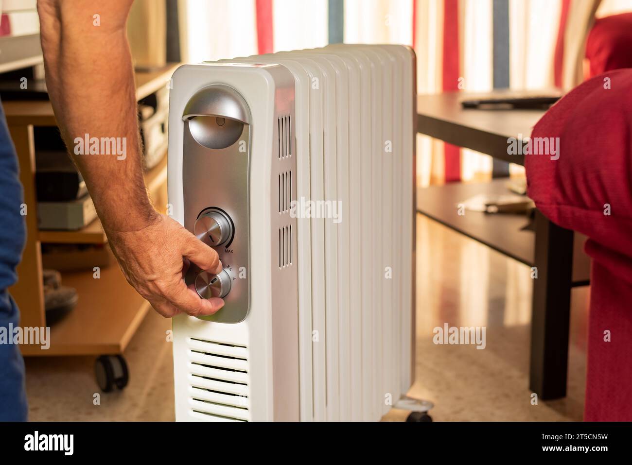 Man's hand selecting the temperature on a home radiator in the living room. Stock Photo