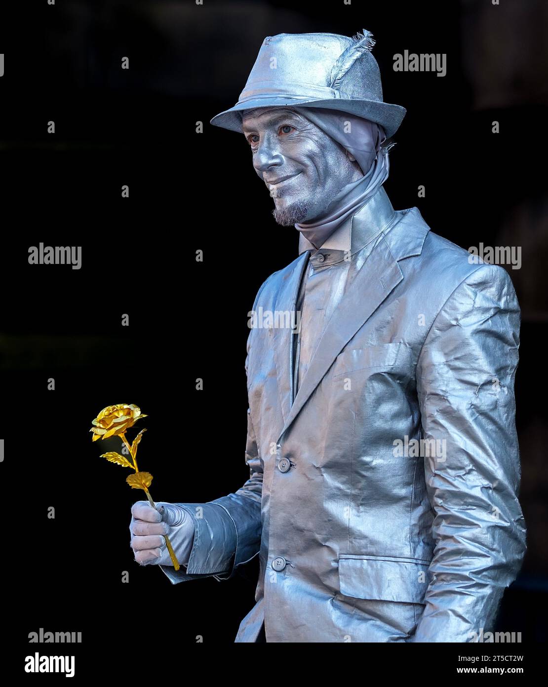 silver painted man with a gold rose pretending to be a statue performing at Edinburgh Fringe, Scotland Stock Photo
