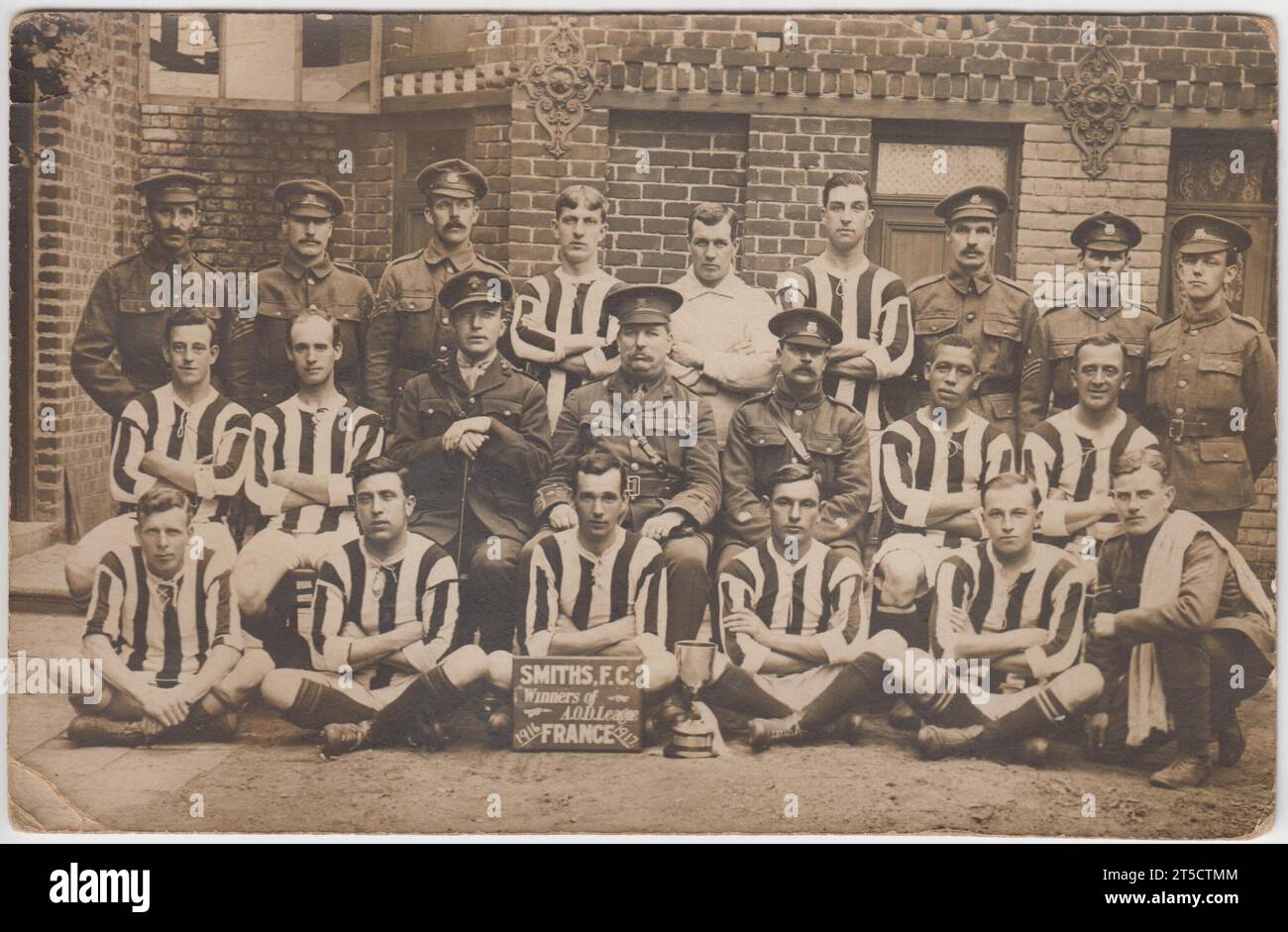Smiths FC, winners of Army Ordnance Department (AOD) League, France, 1916/7: Team photograph of a First World War army football team. It shows a group of men, some in football kit, others in army uniform, posing with a league cup outside a slightly damaged brick building. One of the players (middle row, second from right) is of African or Caribbean origin, another soldier (top row, far left) may also be of non-European ancestry Stock Photo