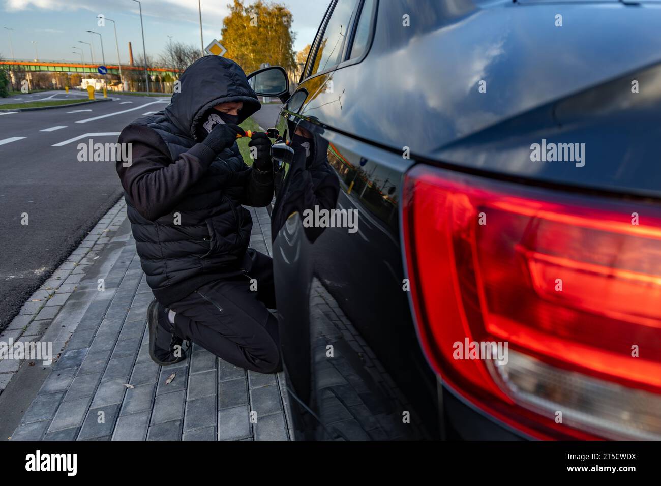 Attempted to steal a car using a suitcase in the city center - a thief in a hood with a mask on his face Stock Photo