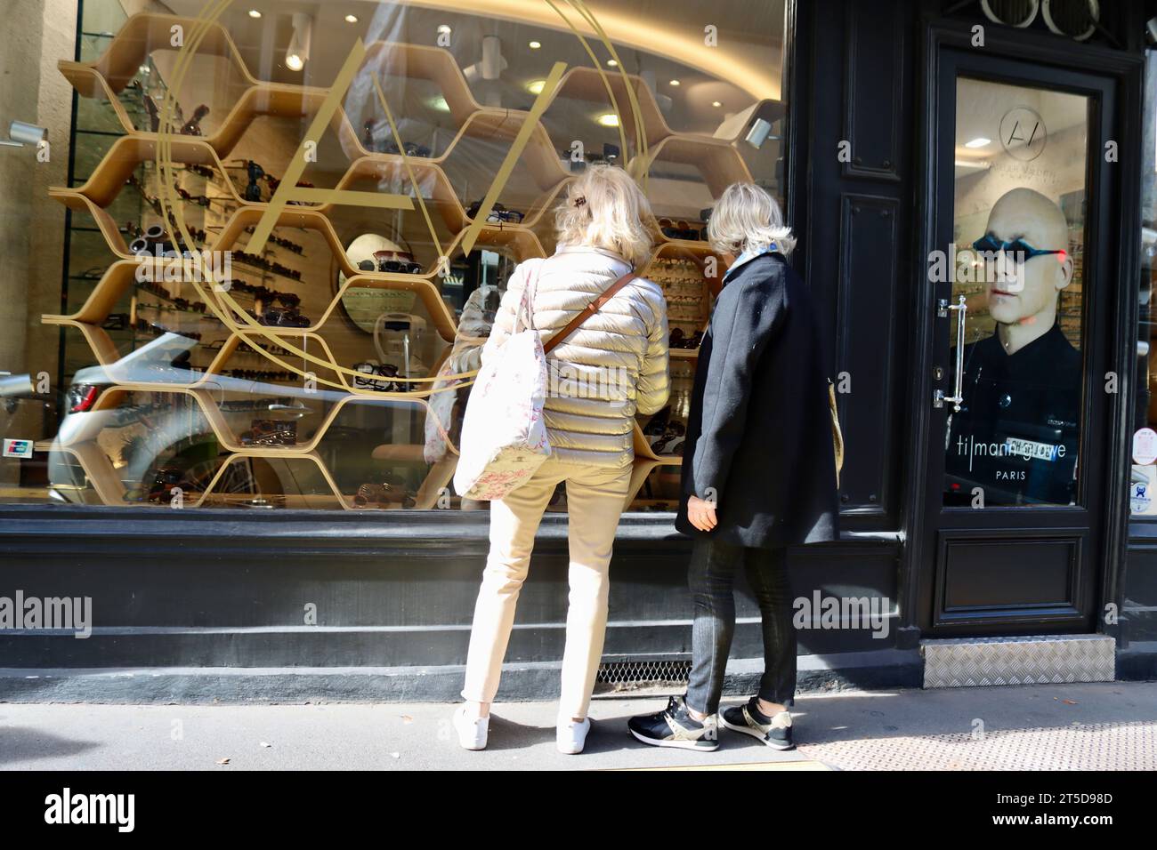 Two window-shoppers outside Atelier Valentin Lunetier with Tilmann Grawe advertising in Paris, France Stock Photo