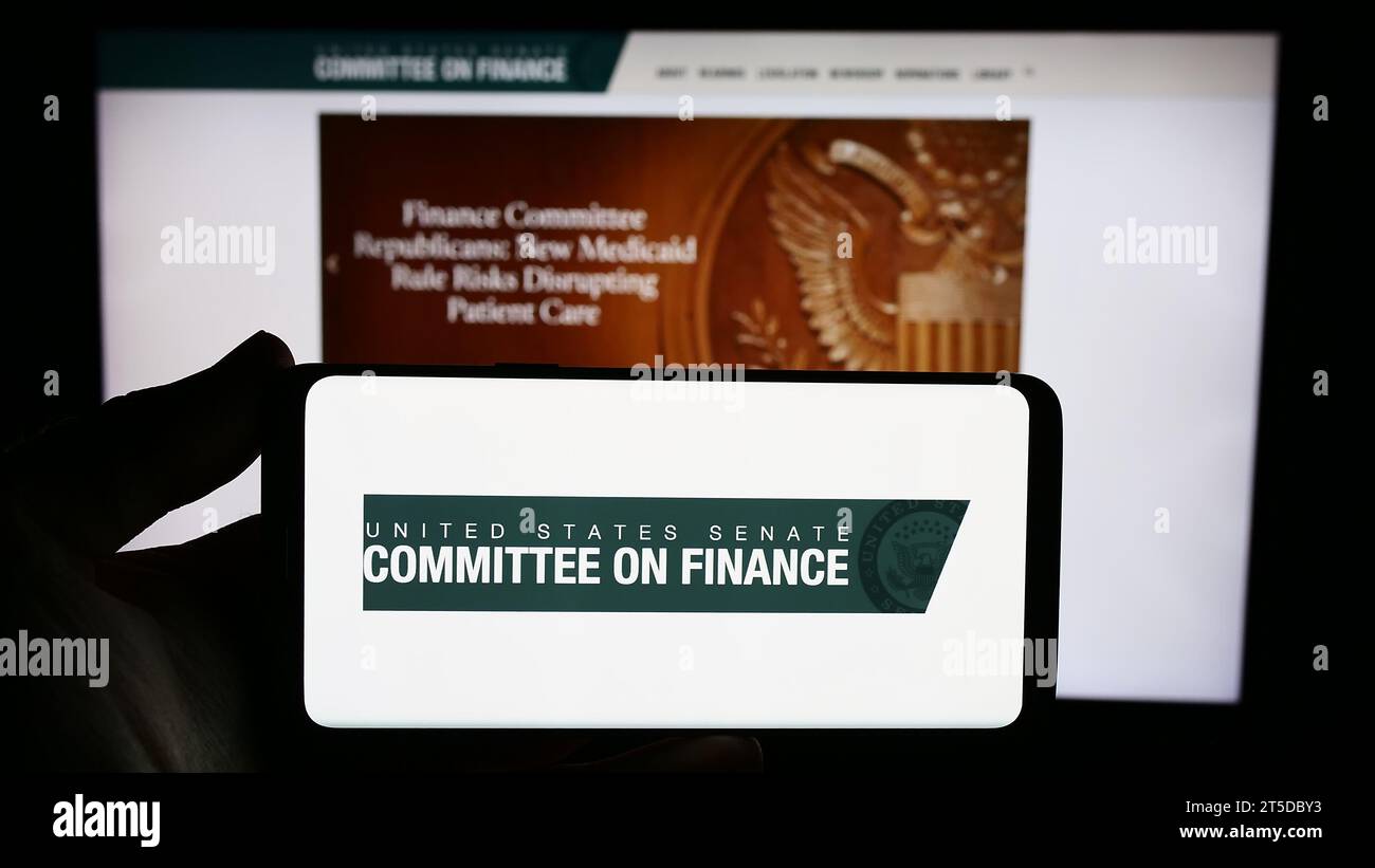 Person holding smartphone with logo of United States Senate Committee on Finance in front of website. Focus on phone display. Stock Photo