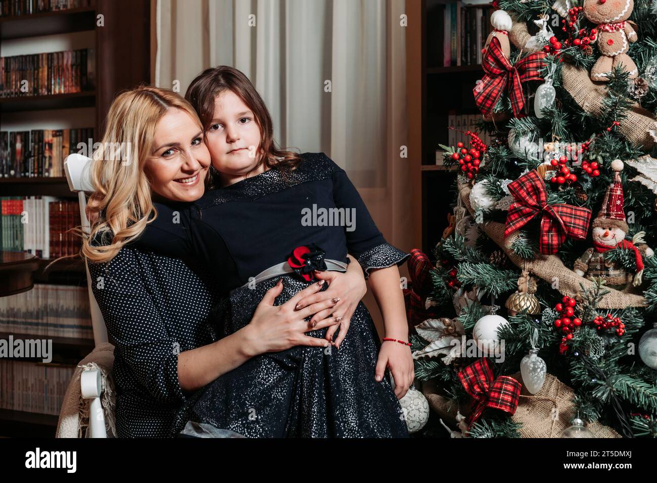 Mother and daughter sitting by the Christmas tree. Family holiday time Stock Photo