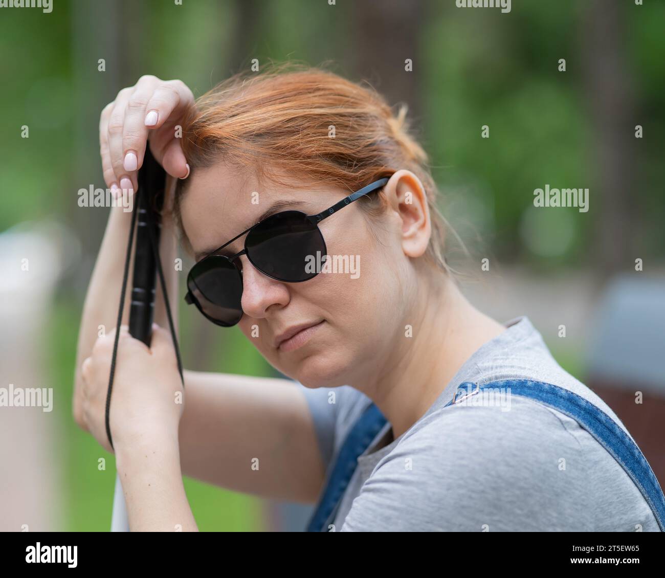 Blind red-haired woman sitting outdoors leaning on a cane.  Stock Photo
