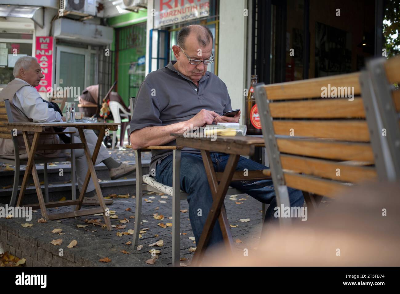 Belgrade, Serbia, Oct 24, 2023: A retired man seated in a pub texting a message Stock Photo