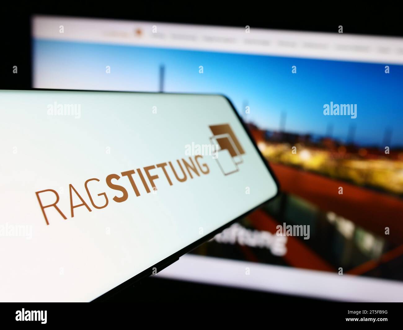 Mobile phone with logo of German foundation RAG-Stiftung in front of website. Focus on center-left of phone display. Stock Photo